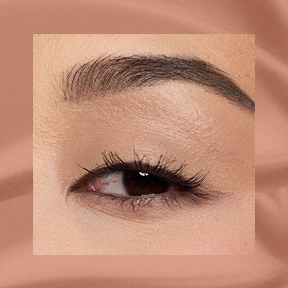 Close-up of an eye area with NYX Professional Makeup Lid Lingerie Cream Eye Pigment in Beige Appeal, shown on a tan matte textured background.