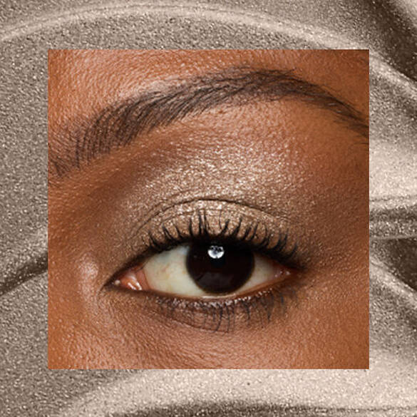 Close-up of an eye area with NYX Professional Makeup Lid Lingerie Cream Eye Pigment in Granite Grind, shown on a brown shimmer textured background.
