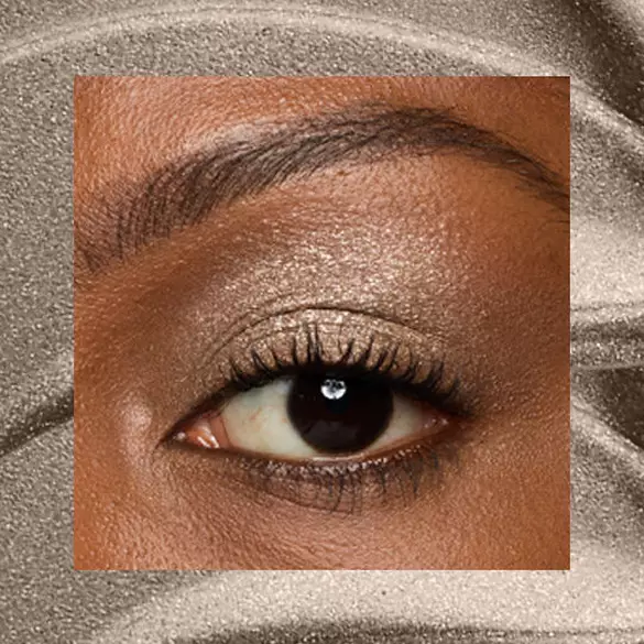Close-up of an eye area with NYX Professional Makeup Lid Lingerie Cream Eye Pigment in Granite Grind, shown on a brown shimmer textured background.