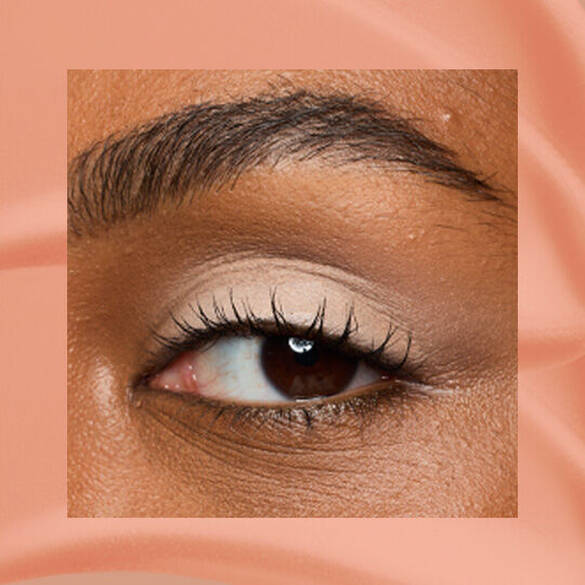Close-up of an eye area with NYX Professional Makeup Lid Lingerie Cream Eye Pigment in In-Nude-Endo, shown on a nude matte textured background.