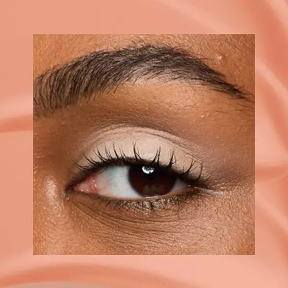 Close-up of an eye area with NYX Professional Makeup Lid Lingerie Cream Eye Pigment in In-Nude-Endo, shown on a nude matte textured background.