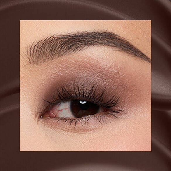 Close-up of an eye area with NYX Professional Makeup Lid Lingerie Cream Eye Pigment in Mocha Mesh, shown on a brown matte textured background.