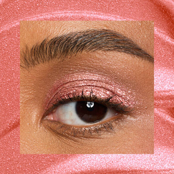 Close-up of an eye area with NYX Professional Makeup Lid Lingerie Cream Eye Pigment in Cheeky Coral, shown on a coral shimmer textured background.