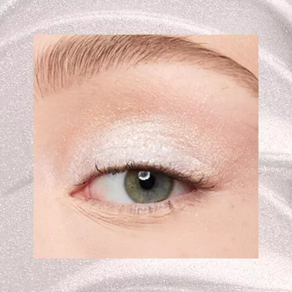 Close-up of an eye area with NYX Professional Makeup Lid Lingerie Cream Eye Pigment in Satin Silver, shown on a shimmering silver textured background.