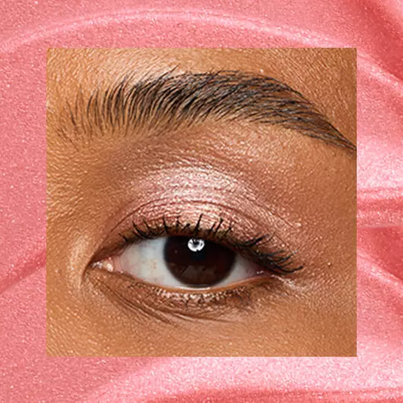 Close-up of an eye area with NYX Professional Makeup Lid Lingerie Cream Eye Pigment in Risky Rose, shown on a rose gold shimmer textured background.